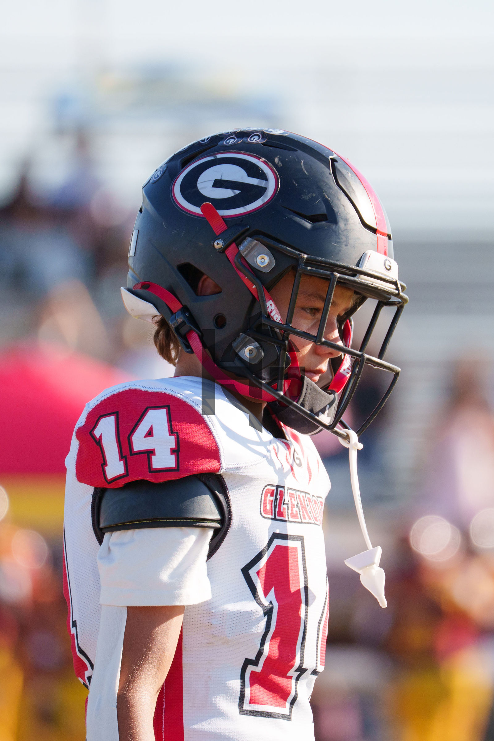 A young football player in a black helmet looks into the camera