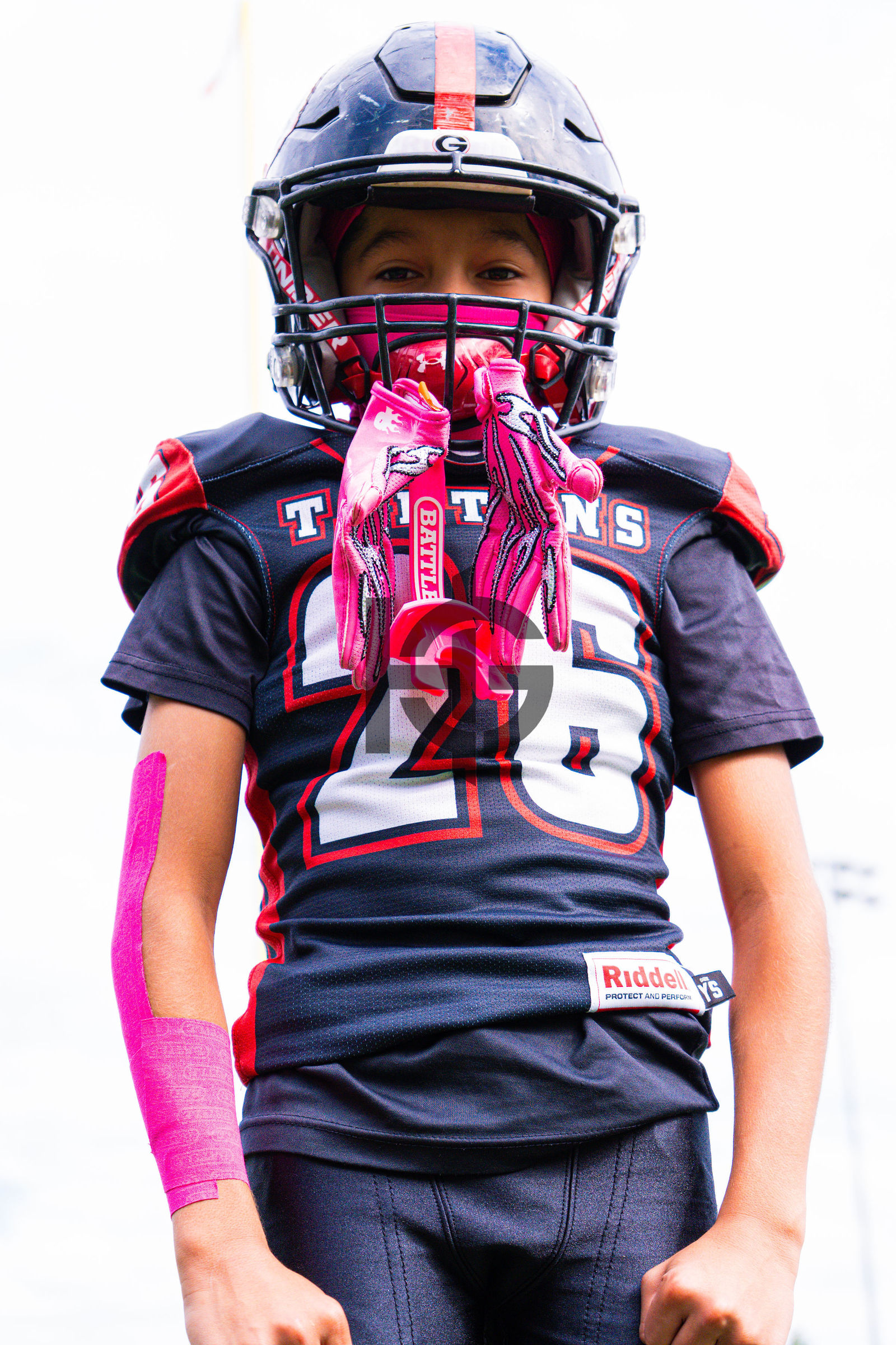 A youth football player in a Titans jersey wearing pink gloves in his facemask